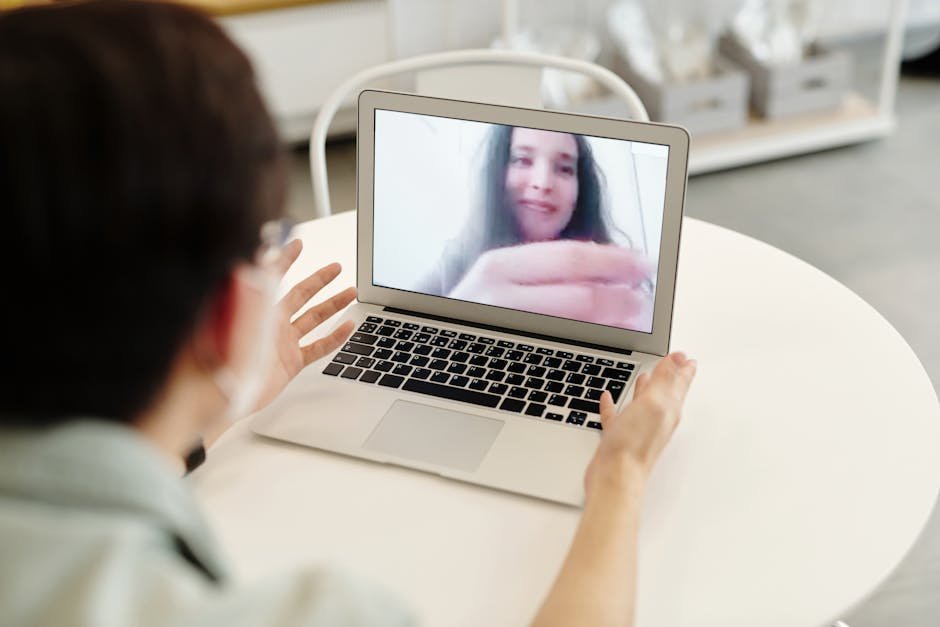 A laptop screen showing a video therapy session interface with a serene interior background, a journal and pen on the desk beside it