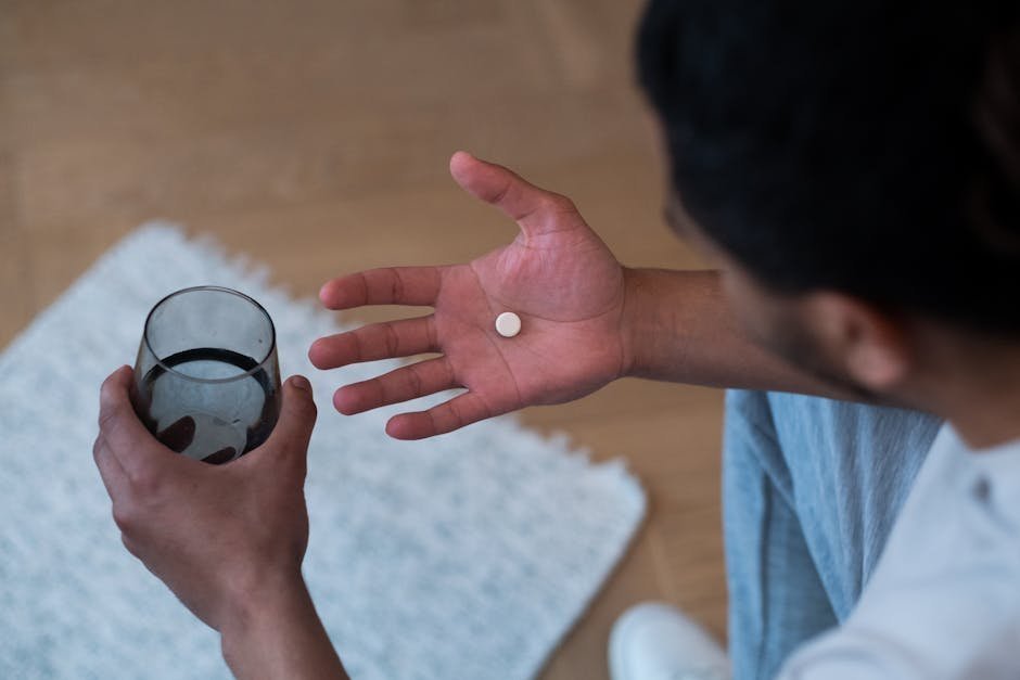 Person holding a glass of water with a single small pill