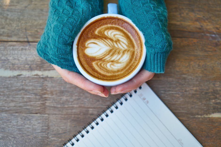 Morning routine for mental health journal and coffee: an open notebook and a warm cup of coffee on a wooden table by a window, the quiet small ritual at the heart of a gentle morning routine for mental health